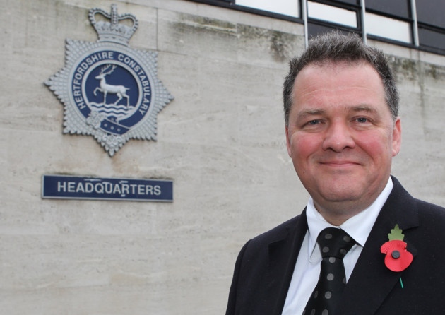 David Lloyd, Police and Crime Commissioner for Hertfordshire, standing in front of a Hertfordshire Police sign