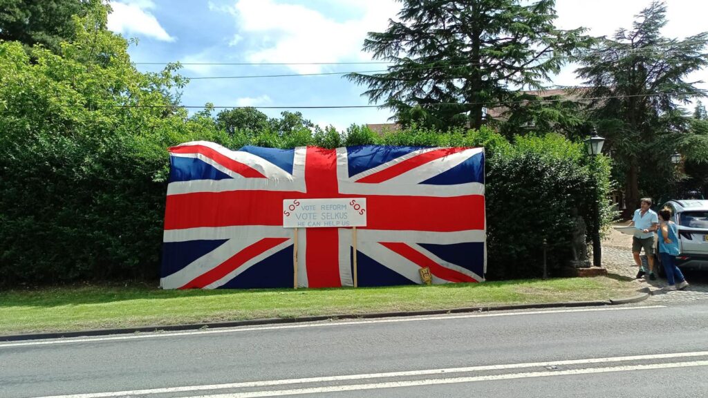 Huge Union flag draped across a hedge outside a house in the Hertsmere constituency. A sign in the middle of the flag reads: 'SOS Vote Reform. Vote Selkus. He can help us'